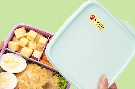 A blue lunchbox with a "Nut Allergy" name label slightly open to reveal healthy foods.